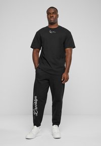 Svart bomull T-skjorte med korte ermer, med en hvit logo på brystet. Kombinert med svarte joggebukser og hvite sneakers.