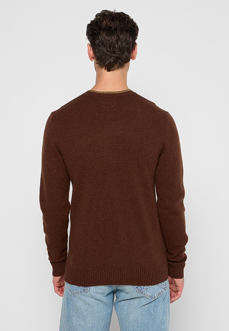 Brauner Strickpullover mit rundem Ausschnitt, gerippten Bündchen und Saum, aus strukturiertem Stoff. Getragen mit hellblauen Jeans.