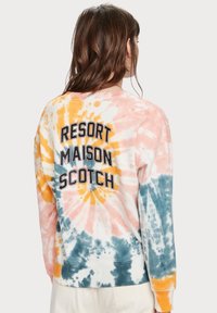 Felpa tie-dye in colori pastello con motivi arancioni, rosa e blu. Sul retro c'è la scritta "RESORT MAISON SCOTCH" in grandi lettere nere.