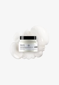 Vit burk märkt "Metal DX" med svart skruvkork, omgiven av vit krämig textur. Innehåller 150 ml professionell hårmask.