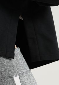 Maglietta nera a maniche corte con orlo dritto, abbinata a leggins grigi con una fascia larga in vita e un dettaglio a striscia grigia chiara.