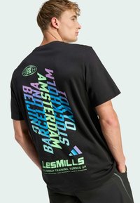 Camiseta negra con gráfico de texto multicolor en la parte trasera, que incluye nombres de ciudades y el logo de "LesMills". Diseño de manga corta y cuello redondo.