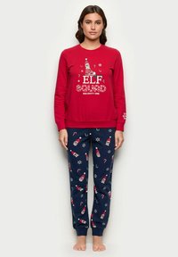 Punavuoren pitkähihainen pyjamapaita, jossa on "ELF SQUAD NAUGHTY ONE" -grafiikka. Meripihkainen pyjamahousu, jossa on tonttu- ja kandypillukuviota. Pehmeä puuvillakangas.