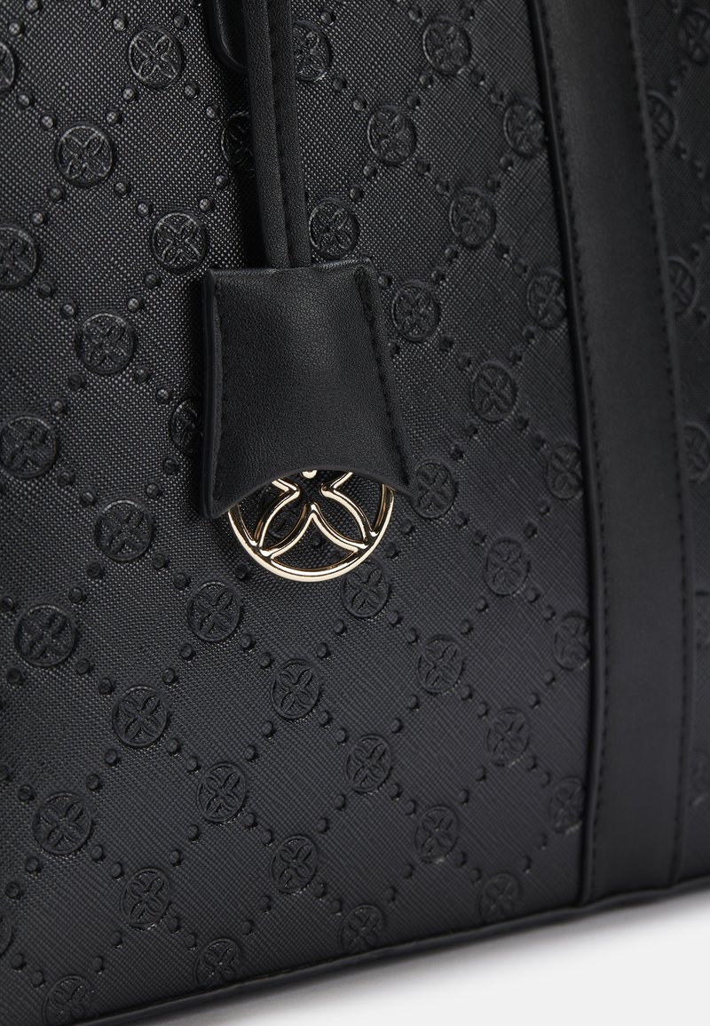 Bolso negro texturizado con un patrón de logo en relieve, detalles de cuero y un adorno circular de hardware dorado. Presenta un diseño estructurado.