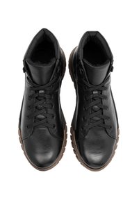 Czarne skórzane buty o teksturowanym wykończeniu, z klasycznym sznurowaniem, wyściełanym kołnierzem i gumowymi podeszwami w kontrastowym brązowym kolorze.