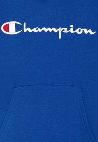 Felpa blu realizzata in morbido tessuto, dotata di una tasca frontale e del logo "Champion" ricamato in bianco con un accento rosso.
