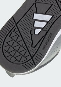 Suela de zapato deportivo gris con superficie de goma texturizada con ranuras diagonales y franjas blancas de acento, etiquetada como "NO DEJA MARCAS."