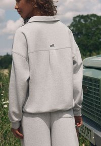 Hall hall, puuvillasegust dressipluus krae ja seljal oleva logoga "self." Vabaaja lõige, soonikkoes mansettide ja õmbluse detailidega.