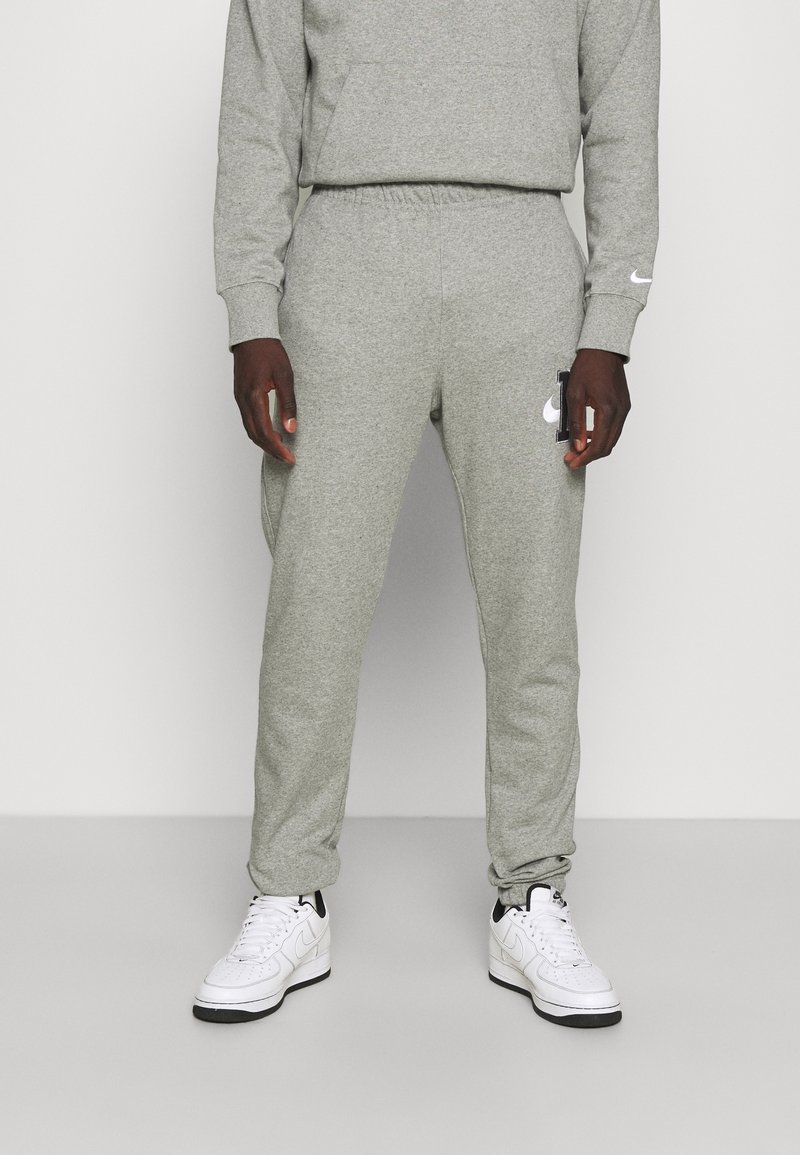 Grå sweatpants tillverkade av mjukt material, med elastisk midja, sidofickor och en vit logotypdetalj på vänster lår.