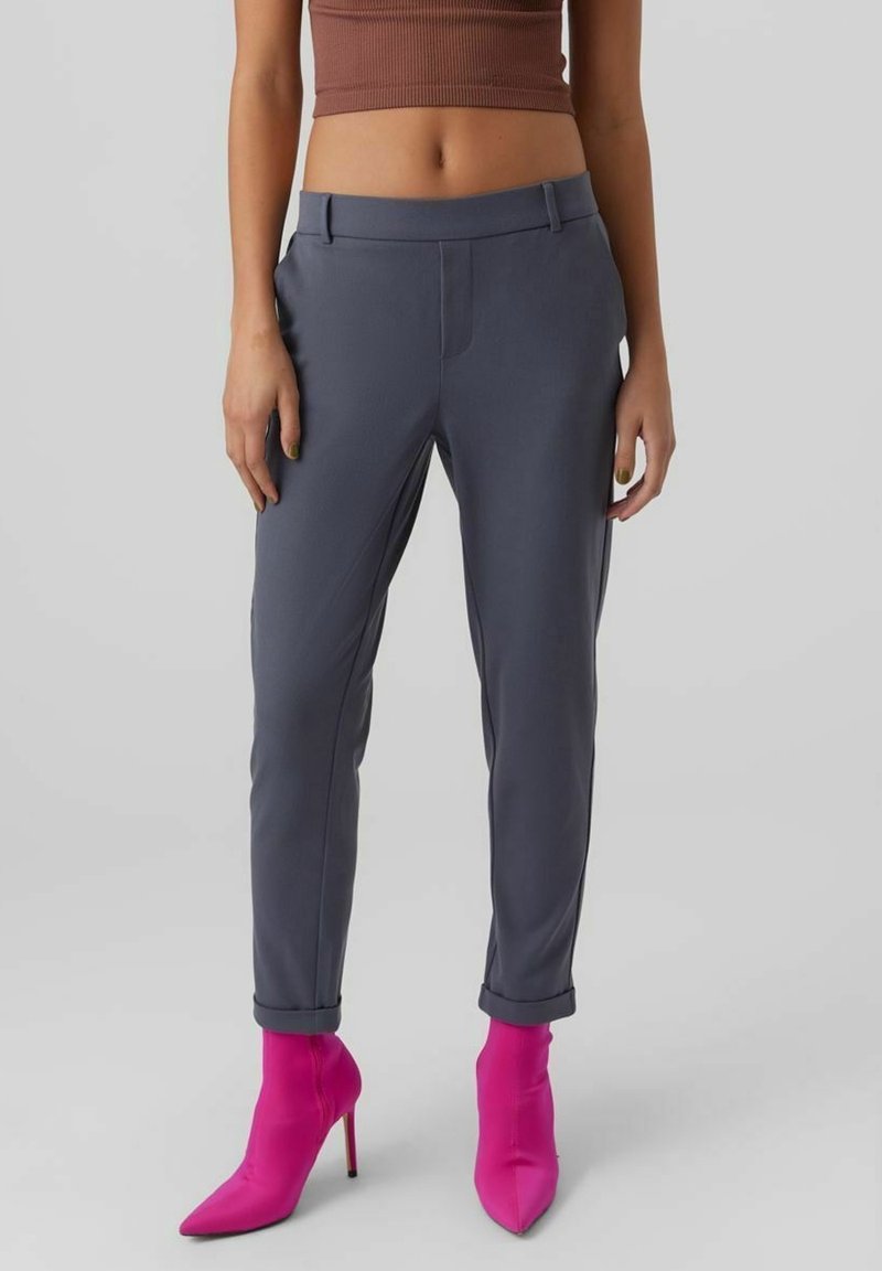Femme portant un pantalon slim gris foncé associé à des bottines à talons hauts rose vif et un top court marron côtelé.