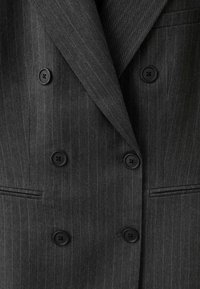 Veste de costume croisée gris foncé à fines rayures avec six boutons noirs et revers crantés, montrant les poches avant et la texture du tissu.