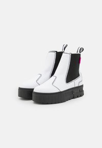 Hvite chelsea-boots med svarte elastiske sider, tykk svart plattformsåle, hvite sømmer og rosa detaljer ved hælen.