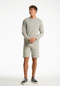 Grå sweatshirt och matchande shorts i mjukt tyg; rund halsringning, långa ärmar, elastiska muddar och midjeresår; avslappnade skor.