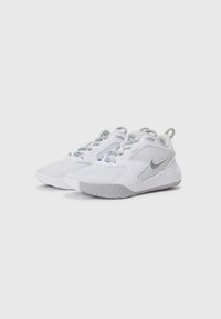 Et par hvite og grå Nike sportsko med lisser, teksturerte såler, og "Just Do It"-tekst på hvit bakgrunn.