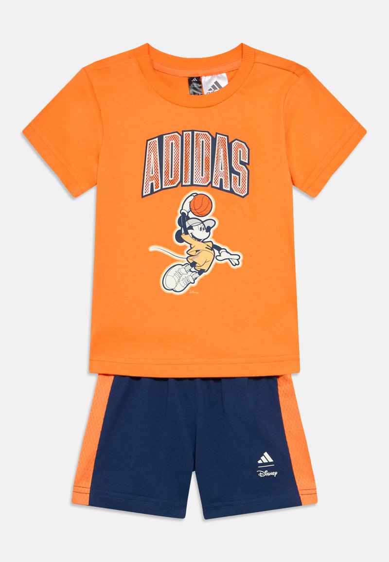 Πορτοκαλί βαμβακερό T-shirt με εκτύπωση "ADIDAS" και γραφικό ενός καρτούν χαρακτήρα. Σκούρα μπλε σορτς με πορτοκαλί διακοσμητικά από δίχτυ και λογότυπο Adidas.