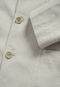 Gestreept shirt in lichtgrijs en wit, met een knoop met vier gaatjes en een zak aan de linkerkant. Katoenstof met een gladde textuur.