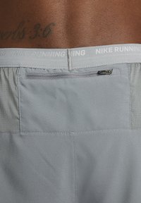 Nike tekaški šortai v svetlo sivi barvi, izdelani iz tkanine, ki odvaja vlago, z zadrgo na zadnjem žepu in strukturo na stranski delu za prezračevanje.