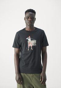 Camiseta de algodón negra con un estampado gráfico de un personaje con un sombrero rojo y una espada azul, combinada con pantalones cortos cargo color oliva.