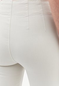 Ljusbeiga, kroppsnära jeans med en mjuk textur och subtila sömdetaljer. Har hög midja och en klassisk femficksdesign.
