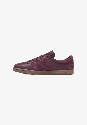Sneaker in pelle bordeaux con lacci abbinati, tre strisce laterali, linguetta in suede sul tallone e suola in gomma marrone testurizzata, orientata verso destra.