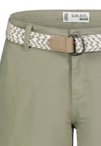 Grüne Baumwollhose mit einem geflochtenen beigen und grauen Gürtel. Zu den Merkmalen gehören eine kreisförmige Metallschnalle und gestickte Details an den Seiten.