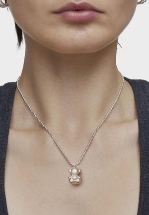 Collar de bola de cadena de plata con un colgante de osito de peluche con acabado brillante y acentos de perlas, descansando sobre un escote neutro.