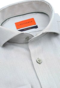Witte shirt met een patroon van een textuurstof, met een gespreide kraag, lichtgrijze knopen en een oranje "Suitable" label. Kwaliteit die niet gestreken hoeft te worden.