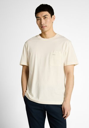 Man draagt een off-white T-shirt met korte mouwen en een borstzakje, staand tegen een effen witte achtergrond.