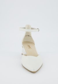 Valge kõrge kontsaga king, millel on pahkluu rihm, terav nina, sile naha tekstuur ja ruudukujuline kontsad. Sisebrändimine nähtav.