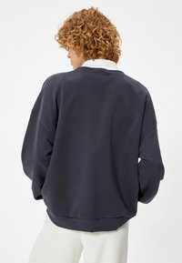 Sudadera de color azul marino oscuro con un corte holgado, dobladillo con ribete y puños. Presenta un cuello blanco en contraste y una textura suave. Se muestra vista trasera.
