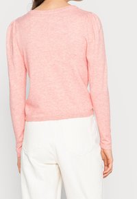 Ljusrosa stickad tröja med långa ärmar, rundad halsringning och ribbad nederkant. Har subtil textur och puffiga axeldetaljer.