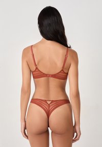 Completo in pizzo rosso con reggiseno e perizoma, in tessuto trasparente, bordi ondulati, spalline regolabili e un piccolo dettaglio di taglio sul perizoma.