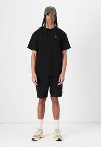 Black cotton t-shirt with short sleeves, paired with black shorts. Worn with a camouflage cap and beige athletic shoes, featuring white socks.