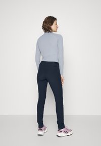 Maglia grigia a maniche lunghe e pantaloni fitted blu navy. La maglia presenta un colletto alto, mentre i pantaloni hanno una texture liscia e una vestibilità su misura. Sneakers rosa completano il look.