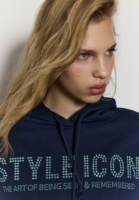 Navy plava majica s kapuljačom s tekstom od cirkona "STYLE ICON" i "UMJETNOST BITI VIDLJIV I ZAPAMĆEN", s vezicama i mekanom teksturom.