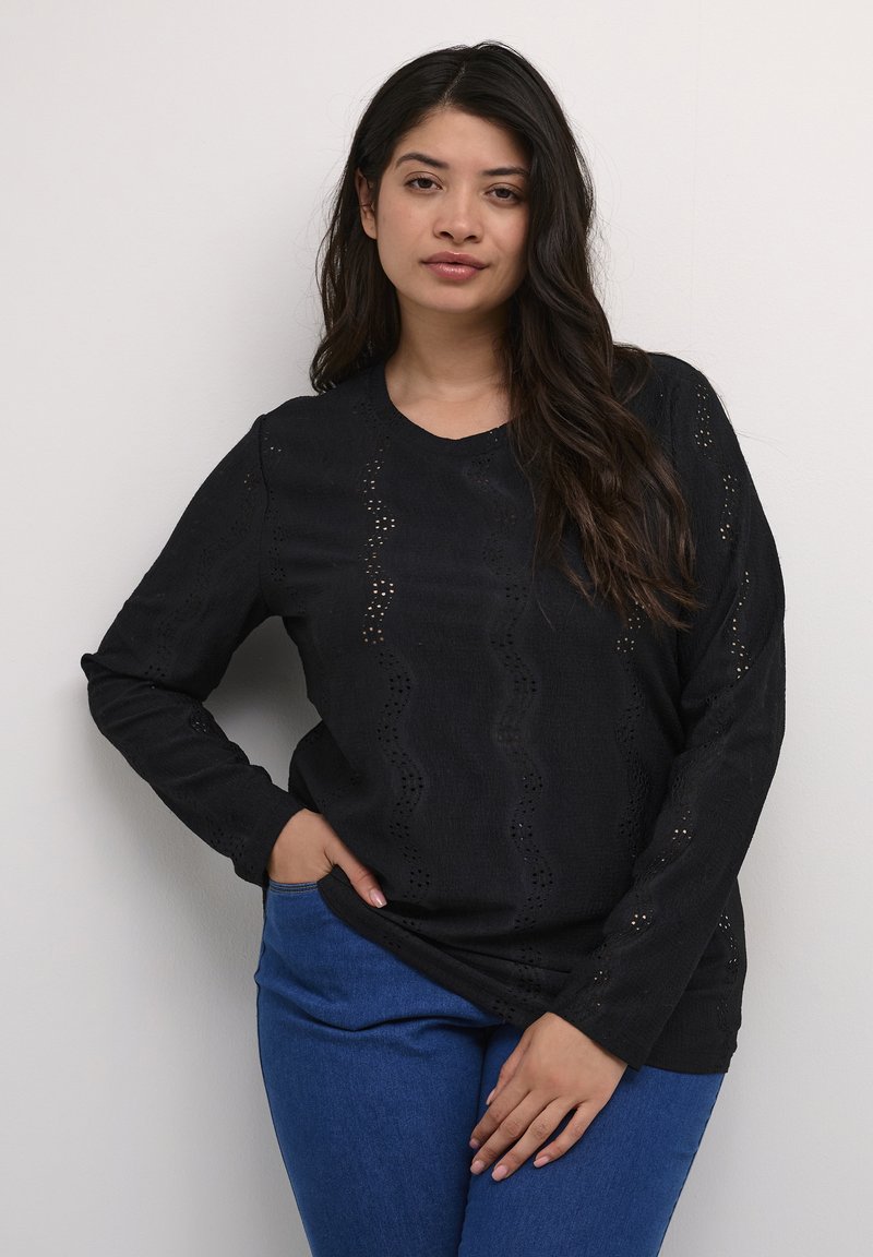 Schwarzer Pullover mit langen Ärmeln, Wellenmuster-Ausschnitten, strukturiertem Stoff und rundem Halsausschnitt. Kombiniert mit blauen Jeans.