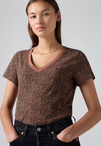 Brun leopardmønster t-skjorte med v-hals og korte ermer. Har en kontrasterende brun kant og en liten rød logo på brystet.