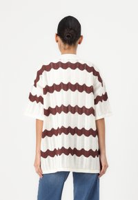 Top overdimensionato a maniche corte in crema con righe ondulate bordeaux. Caratterizzato da una texture a coste e una vestibilità ampia.