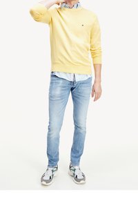 Gul bomuldsstriktrøje, lyseblå knap-op skjorte under, lyseblå jeans, grå og grønne sneakers med kraftige såler.