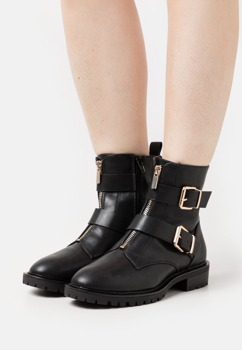 Bottes en cuir noir à la cheville avec deux fermetures éclair latérales, brides ajustables et boucles dorées, dotées d'une semelle en caoutchouc texturée.