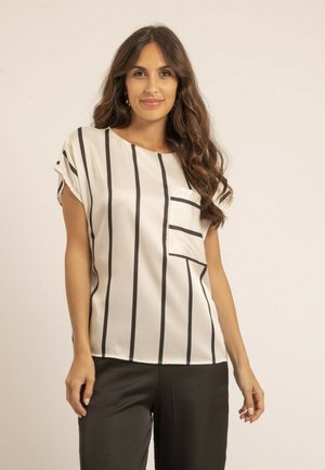 Blouse crème avec des rayures verticales noires, manches courtes retroussées, encolure ronde et poche à l'avant. Tissu lisse avec une légère brillance.