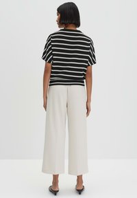 Zwart-wit gestreept, kort mouwen topje, gecombineerd met crèmekleurige, hoge taille wijde broek en zwarte muiltjes, gezien vanuit de achterkant.