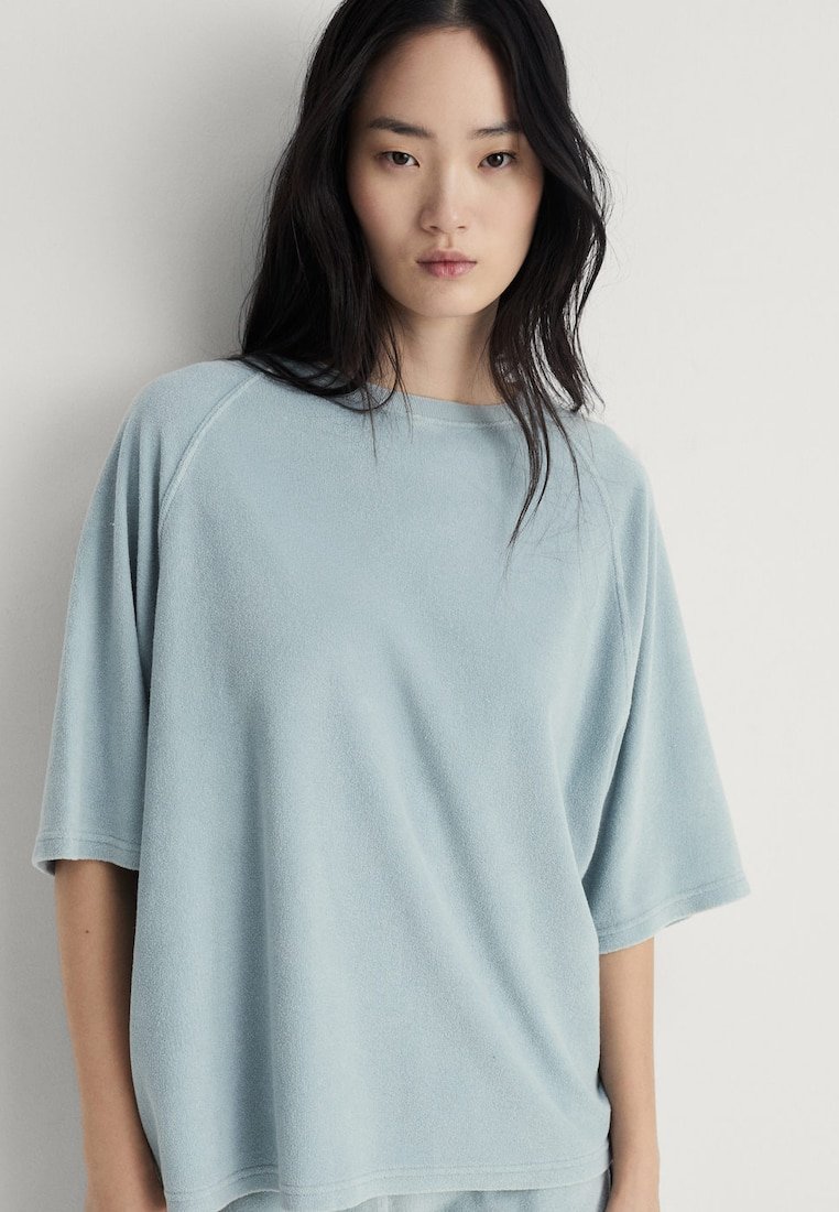 Maglietta in pile oversized di colore azzurro chiaro con maniche raglan corte e colletto rotondo. Tessuto morbido e vestibilità rilassata.