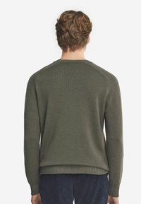 Olivgrön stickad tröja med långa ärmar och ribbad nederkant. Har rundad halsringning och slät textur som visar en enkel, klassisk design.