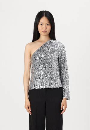 Top en sequins argentés avec design à une épaule et manches longues, présentant une surface texturée et une silhouette ajustée. Associé à un pantalon noir.