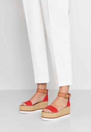 Røde kilehæl sandaler med en espadrille-inspireret jute sål, der har en tan ankelrem og et åbent tådesign, placeret foran en neutral baggrund.