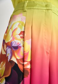 Helle gelbe und pinke plissierte Hosen mit einem floralen Design, das große Rosen und einen Farbverlauf zeigt, betonen lebendige Farbtöne und eine glatte Textur.