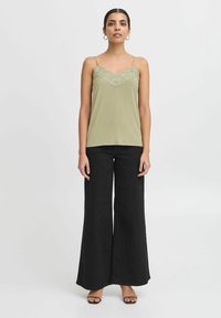 Camisola verde oliva con pizzo, spalline sottili, abbinata a pantaloni neri a gamba larga. Tessuto liscio con vestibilità rilassata.