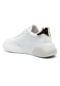 Sneaker in pelle bianca con suola spessa bianca, un accento metallico dorato sul tallone e dettagli di design minimalisti sui lati.