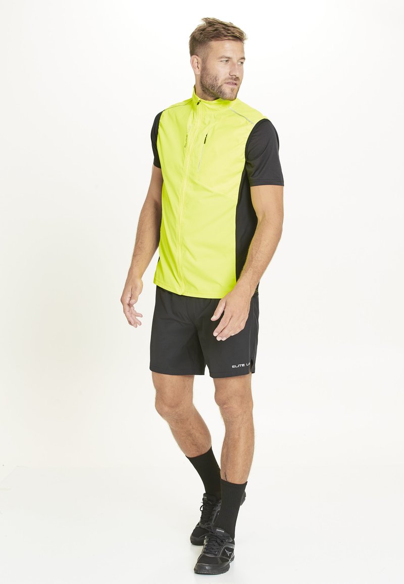 Männervolles Athletic-Weste in leuchtendem Neon-Gelb mit schwarzen kurzen Ärmeln, Frontreißverschluss, kombiniert mit schwarzen Shorts und sportlichen Schuhen, geeignet für sportliche Aktivitäten.